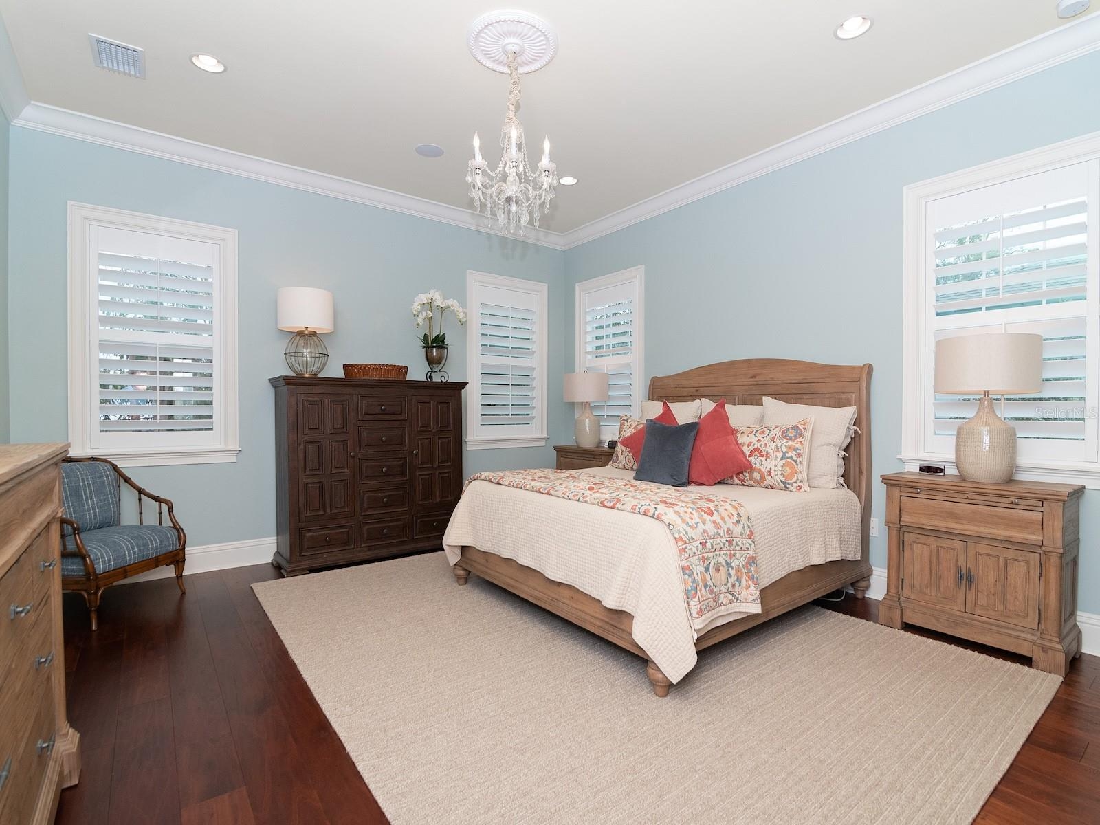 Spacious primary bedroom with plantation shutters, wood floors and crown moulding.