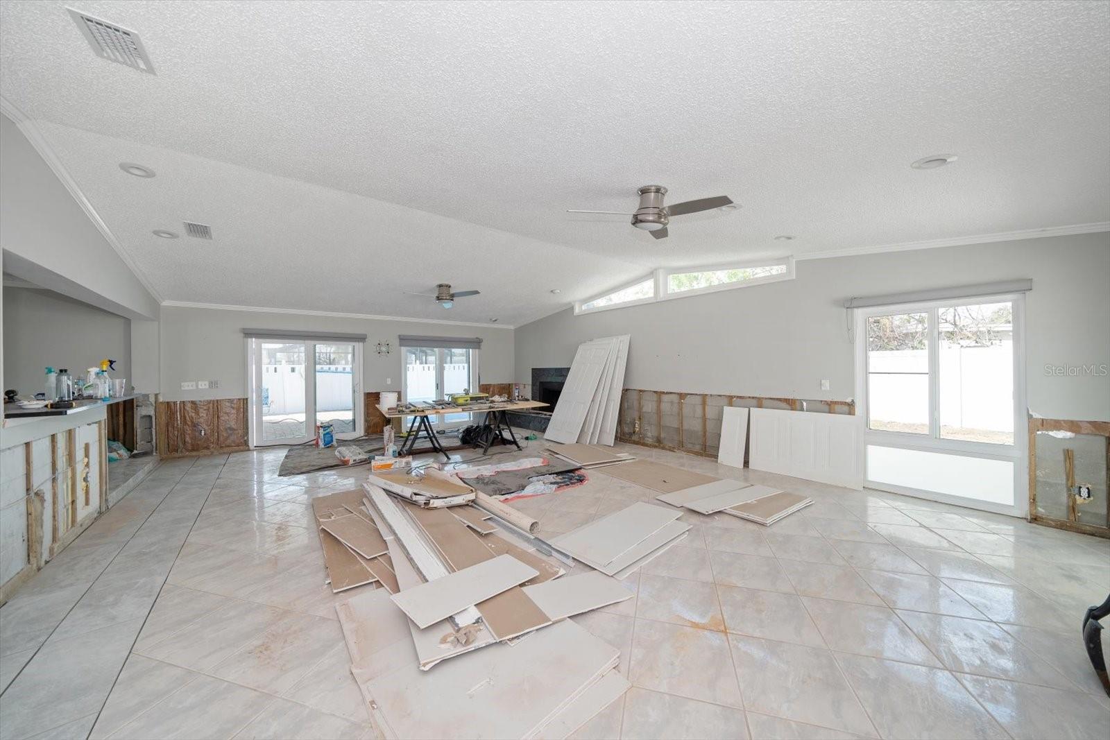 Great Room with high breakfast bar to the left,  new tile, hurricane impact rated sliders and windows and fireplace. Drywall to be installed, textured and painted