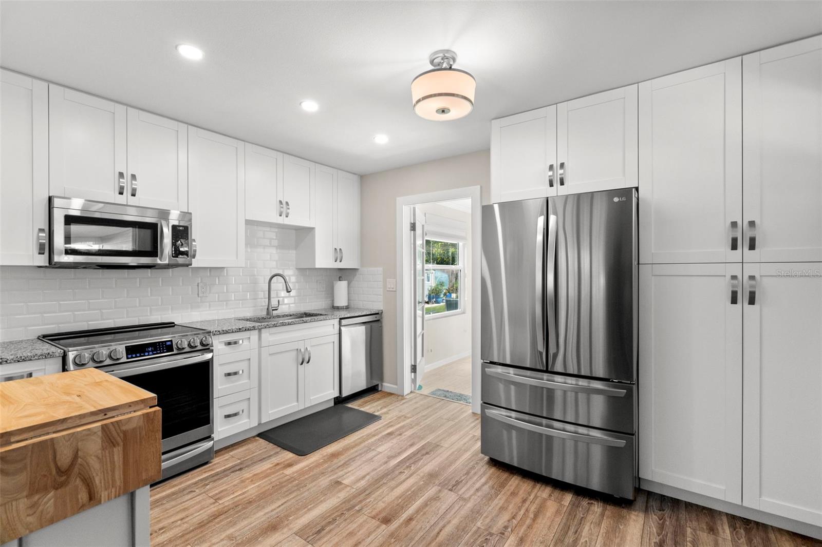 Extended wood shaker cabinetry with soft close drawers, a stand-alone pantry, stainless steel appliances, granite countertops, a chic backsplash and modern lighting.