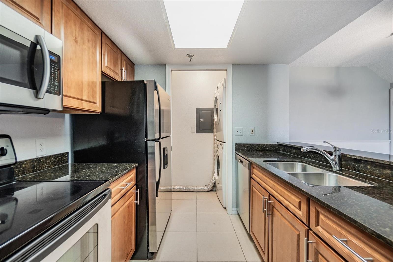 Gally kitchen overlooking dining room with stainless steel appliances, striking countertops, and access to washer and dryer.