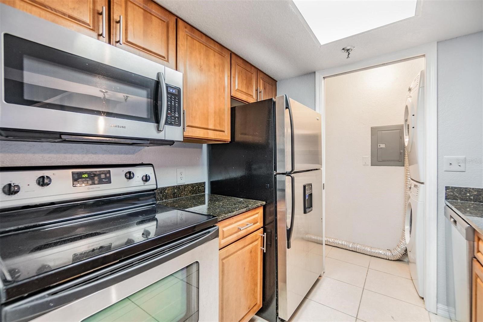 Gally kitchen overlooking dining room with stainless steel appliances, striking countertops, and access to washer and dryer.