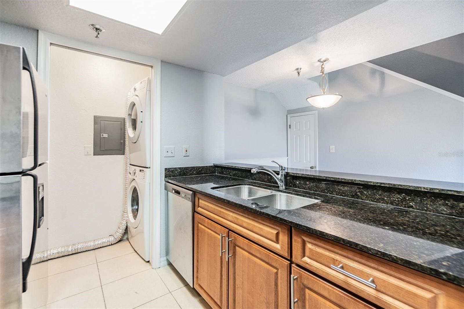 Gally kitchen overlooking dining room with stainless steel appliances, striking countertops, and access to washer and dryer.