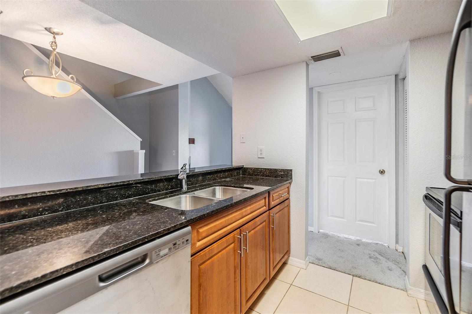 Gally kitchen overlooking dining room with stainless steel appliances, striking countertops, and access to washer and dryer.