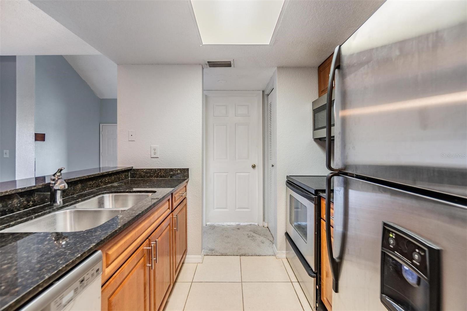 Gally kitchen overlooking dining room with stainless steel appliances, striking countertops, and access to washer and dryer.