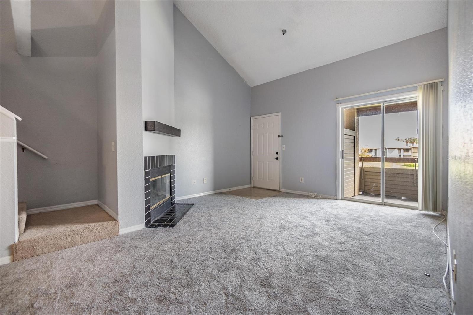 Living room with high open ceiling featuring a cozy fireplace and sliders out to the second floor balcony.