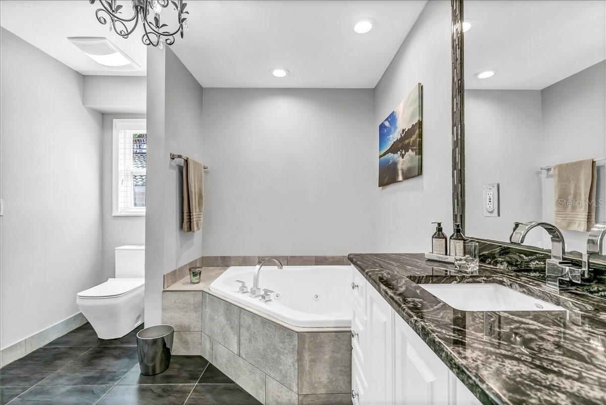 The primary bathroom is equipped with recessed lighting and a spacious ledge near the bathtub, providing an ideal spot for placing your book, wine, or an array of candles.