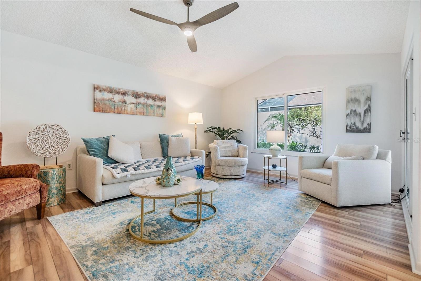 Open living room with vaulted ceilings, beautiful floors, and many windows and sliders for a bright, spacious, and inviting atmosphere