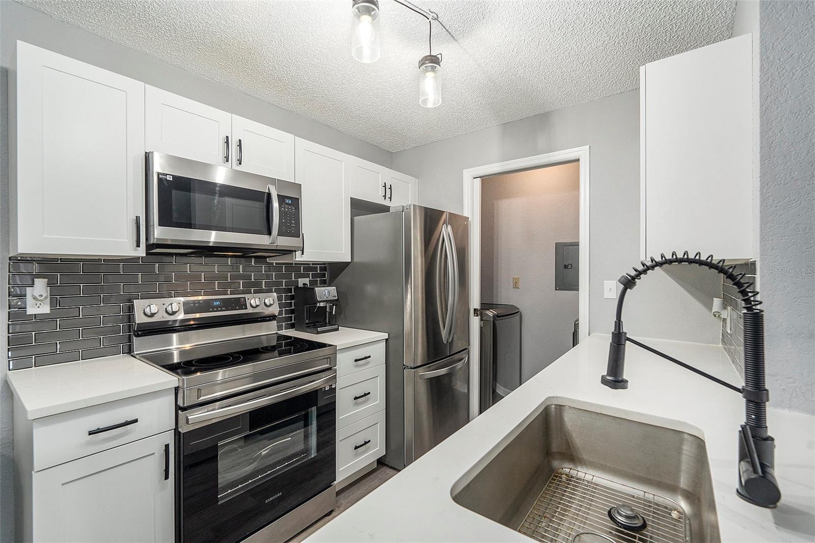 Quartz kitchen countertop, modern tile backsplash, white shaker cabinets, and stainless steel appliances!