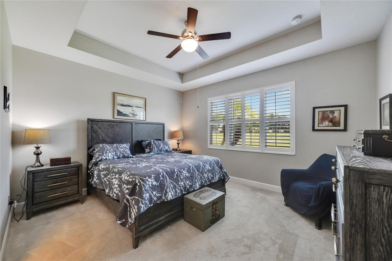 Large primary bedroom with tray ceiling and plantation shutters