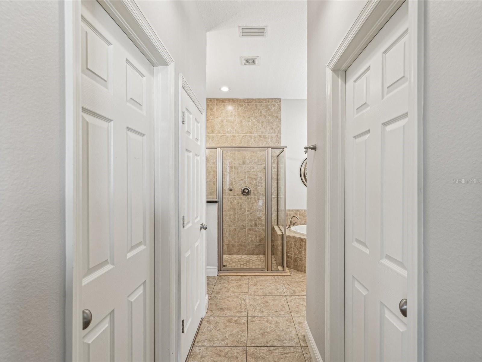 Dual walk-in closets anchor the entry to the bathroom.