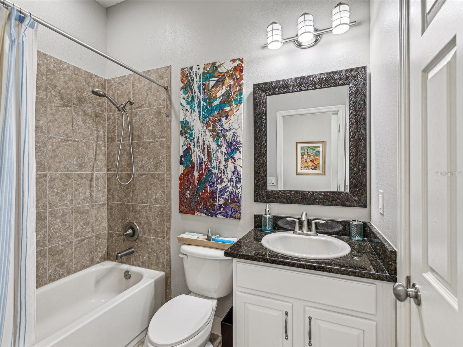 This ensuite bathroom features a tub/shower combination with new lighting, a granite countertop sink and storage and a walk-in closet.