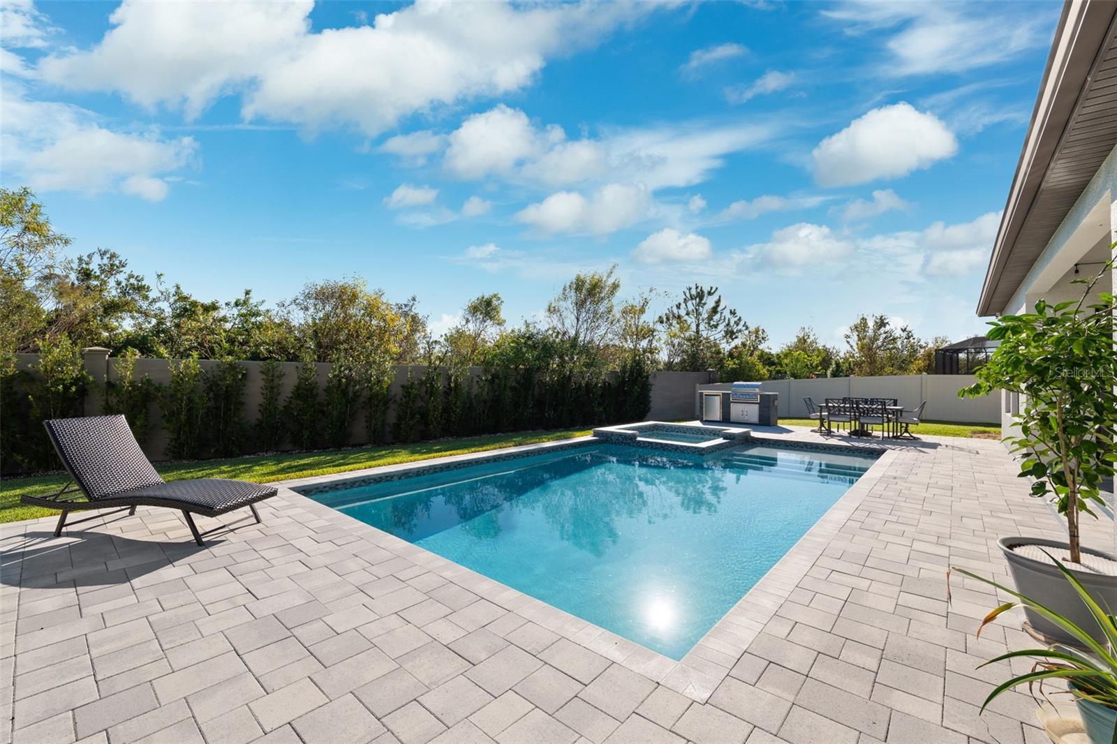 Oversized pool and spa on an open paver deck.