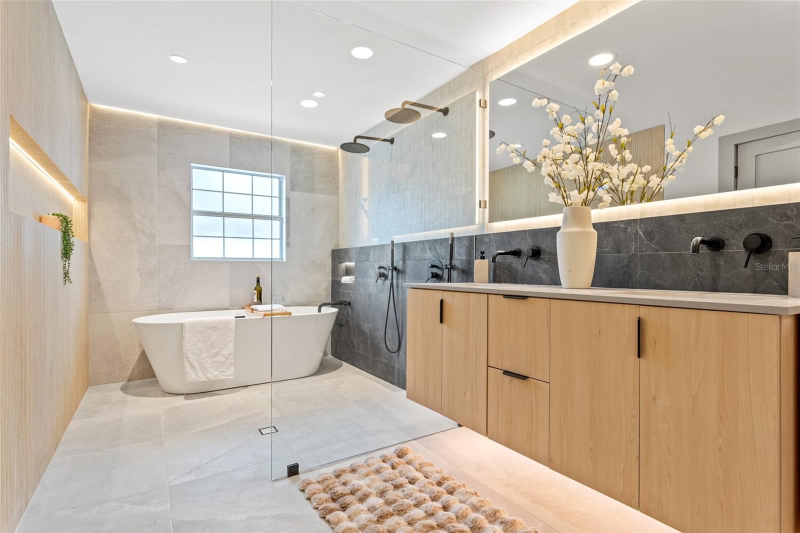 This elegant and luxurious bathroom features a European floating cabinet, a tub with dual shower heads, LED lighting throughout, and multiple niches.