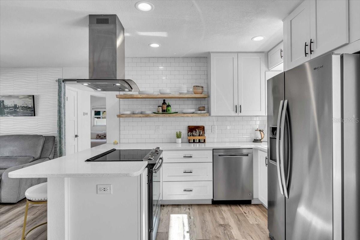 Subway tile to the ceiling with live edge shelving, stainless appliances and single sink.