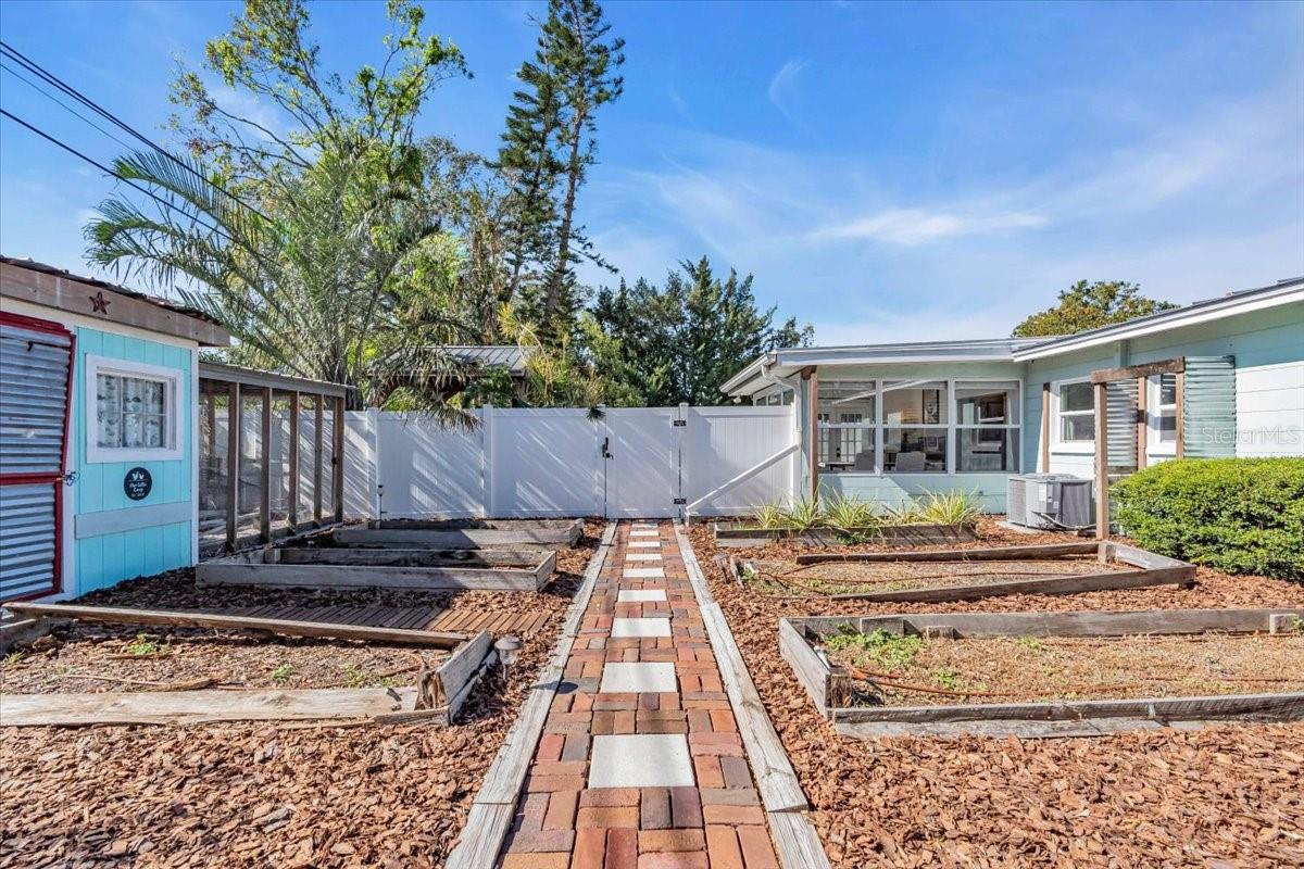 Separate section of back yard is set up with 8 raised planter beds with a drip system, fruit tree, Plumeria and a chicken coup turned into a shed.