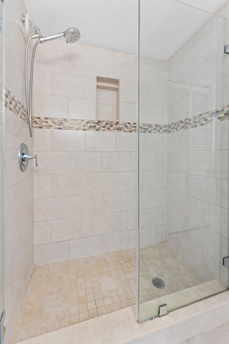 Beautifully tiled glass enclosed shower in the primary suite bathroom.