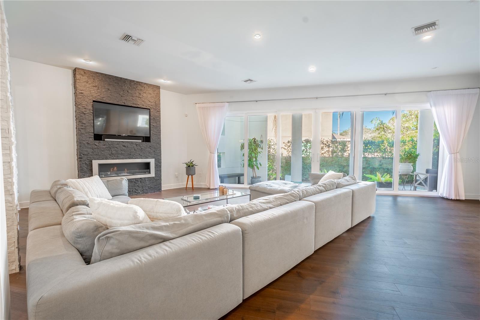 A wall of sliding doors perfectly frames the tropical oasis beyond, showcasing the saltwater heated pool, spa, and serene private patio.