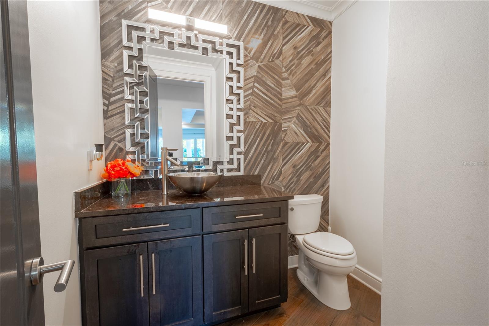 1st Floor powder room features and artistic accent wall, a framed mirror that is a work of art and a rich, dark wood vanity with vessel sink.