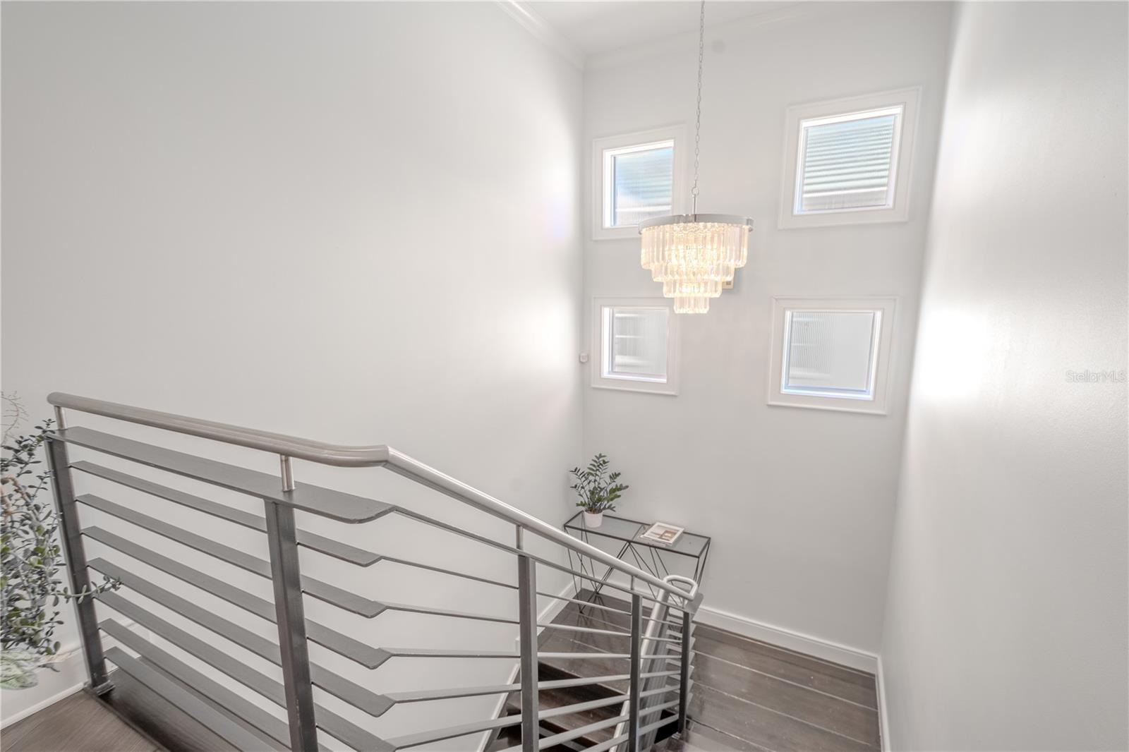 A chandelier hangs in the stairway landing with 4 windows adding natural light.