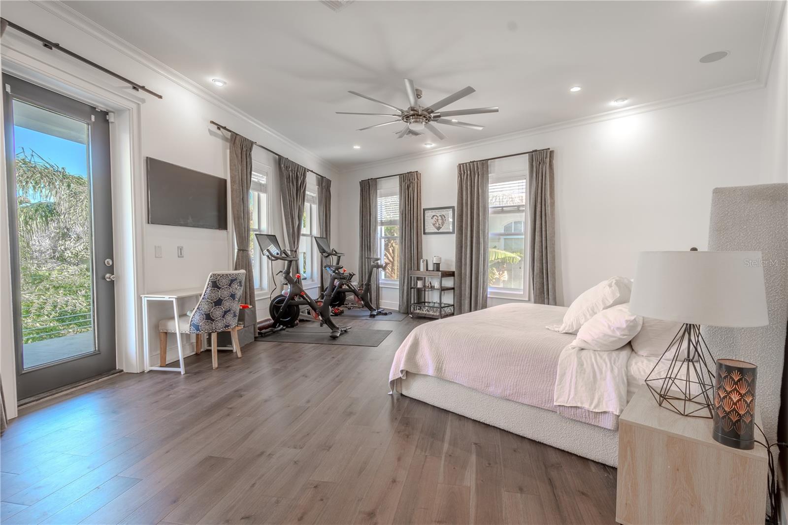 Relax in style: a modern ceiling fan, wood floors, and poolside views elevate this luxurious primary bedroom.