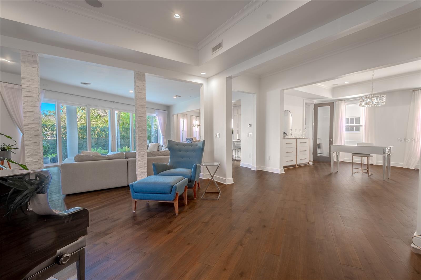 The living room, seamlessly connected to the dining and family rooms, showcases elegant tray ceilings, recessed lighting, and warm wood floors. Its neutral color palette provides a versatile backdrop, making it the perfect space for a grand piano or a cozy conversation area.