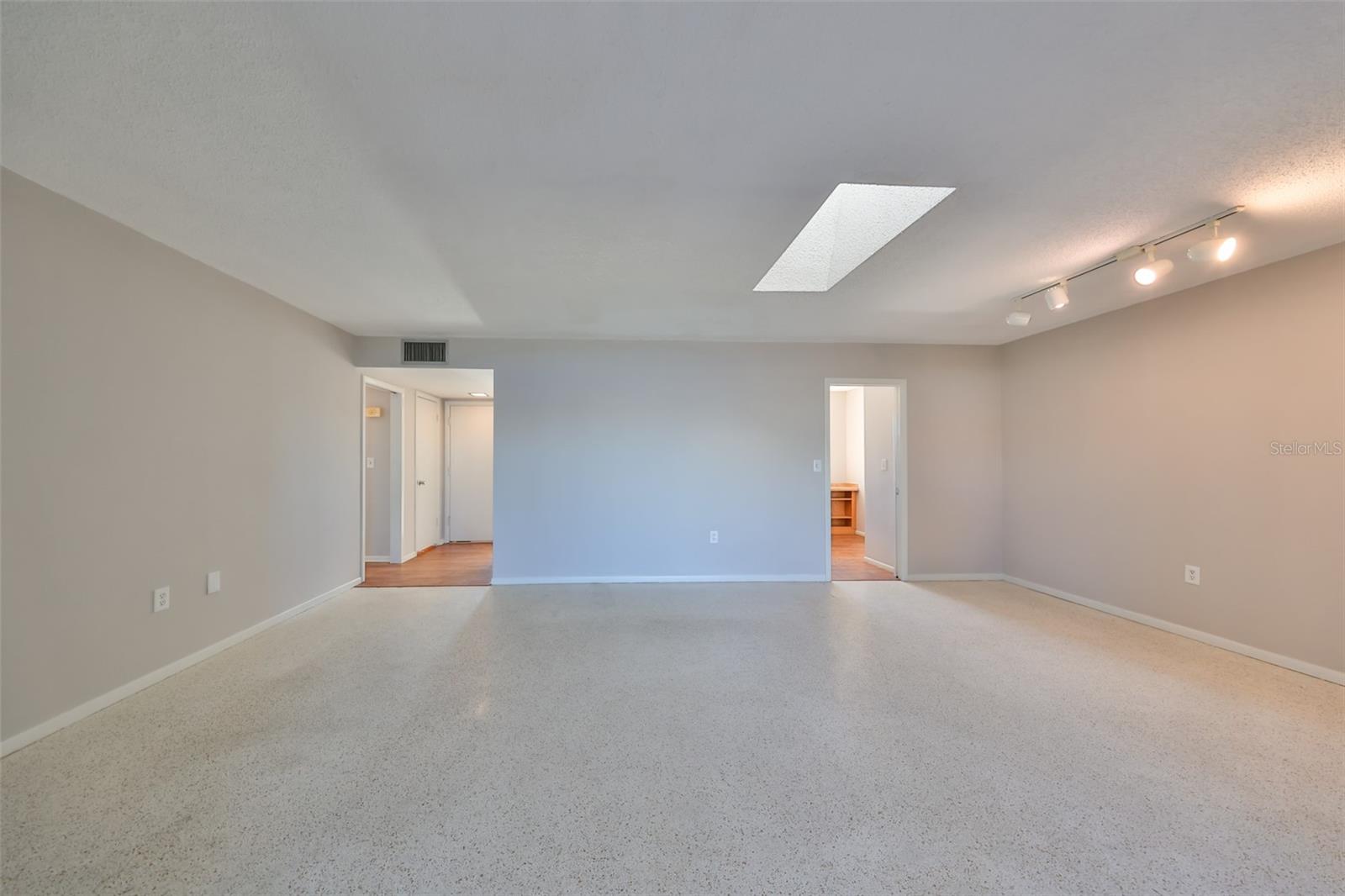 Great Room; living area on left, dining area under track lights, skylight, foyer left rear, pocket door to kitchen, right rear