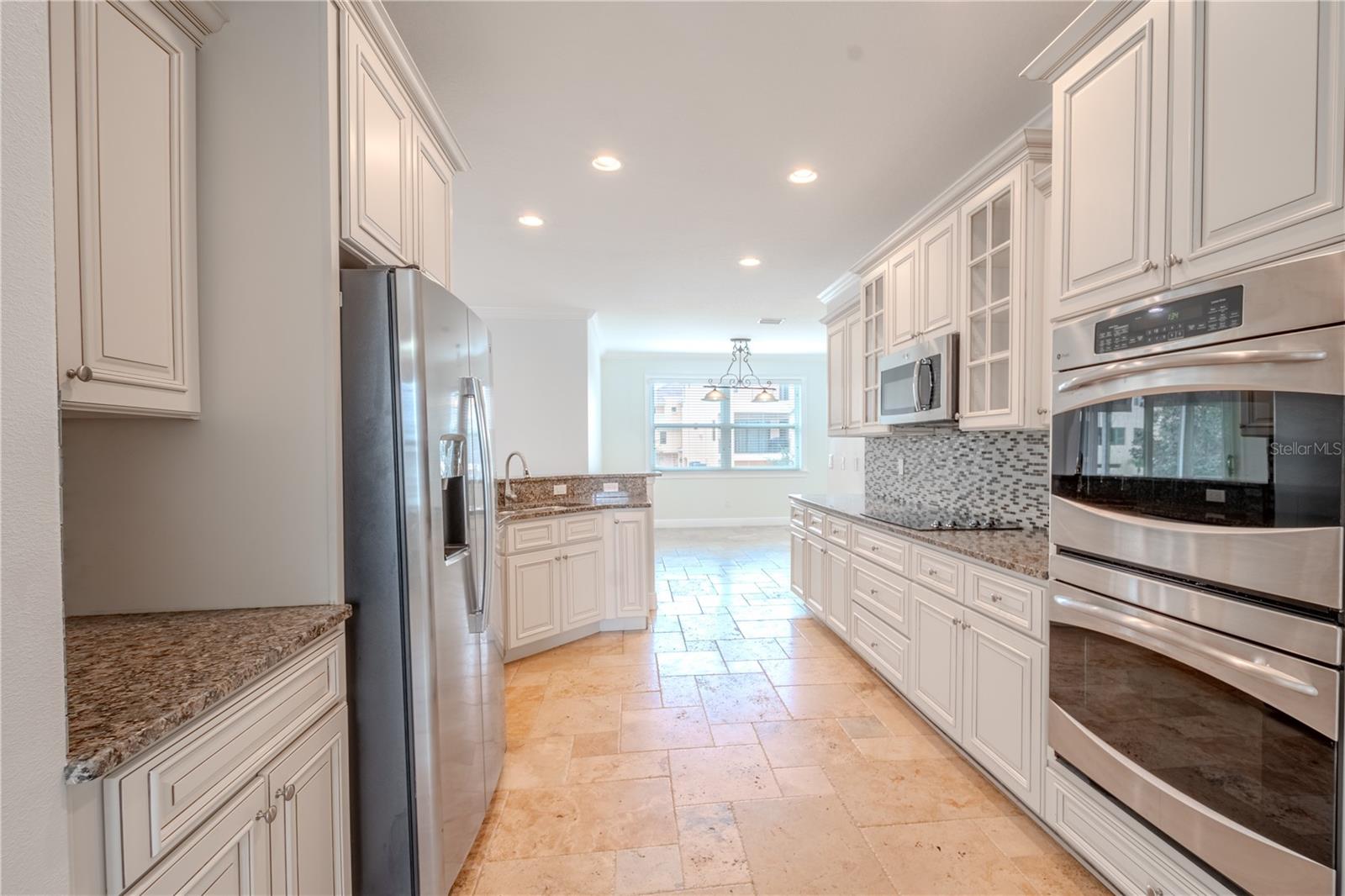 A suite of stainless steel appliances include a convection double oven, a French door refrigerator with ice maker and water dispenser, dishwasher, glass cooktop and microwave.