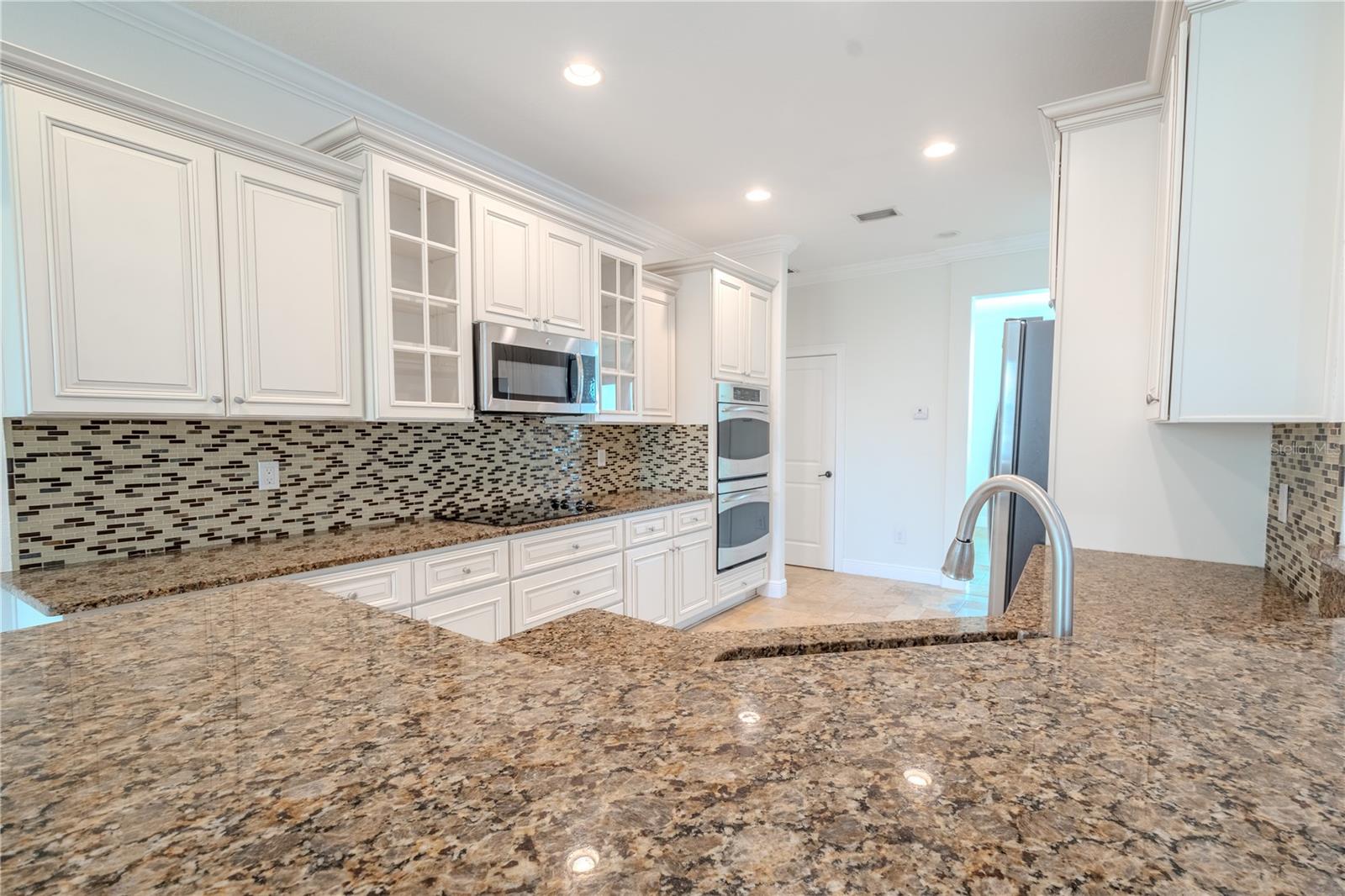 The luxurious granite countertops and the shimmering glass tile backsplash come together to create a striking and elegant centerpiece, blending durability with refined style.