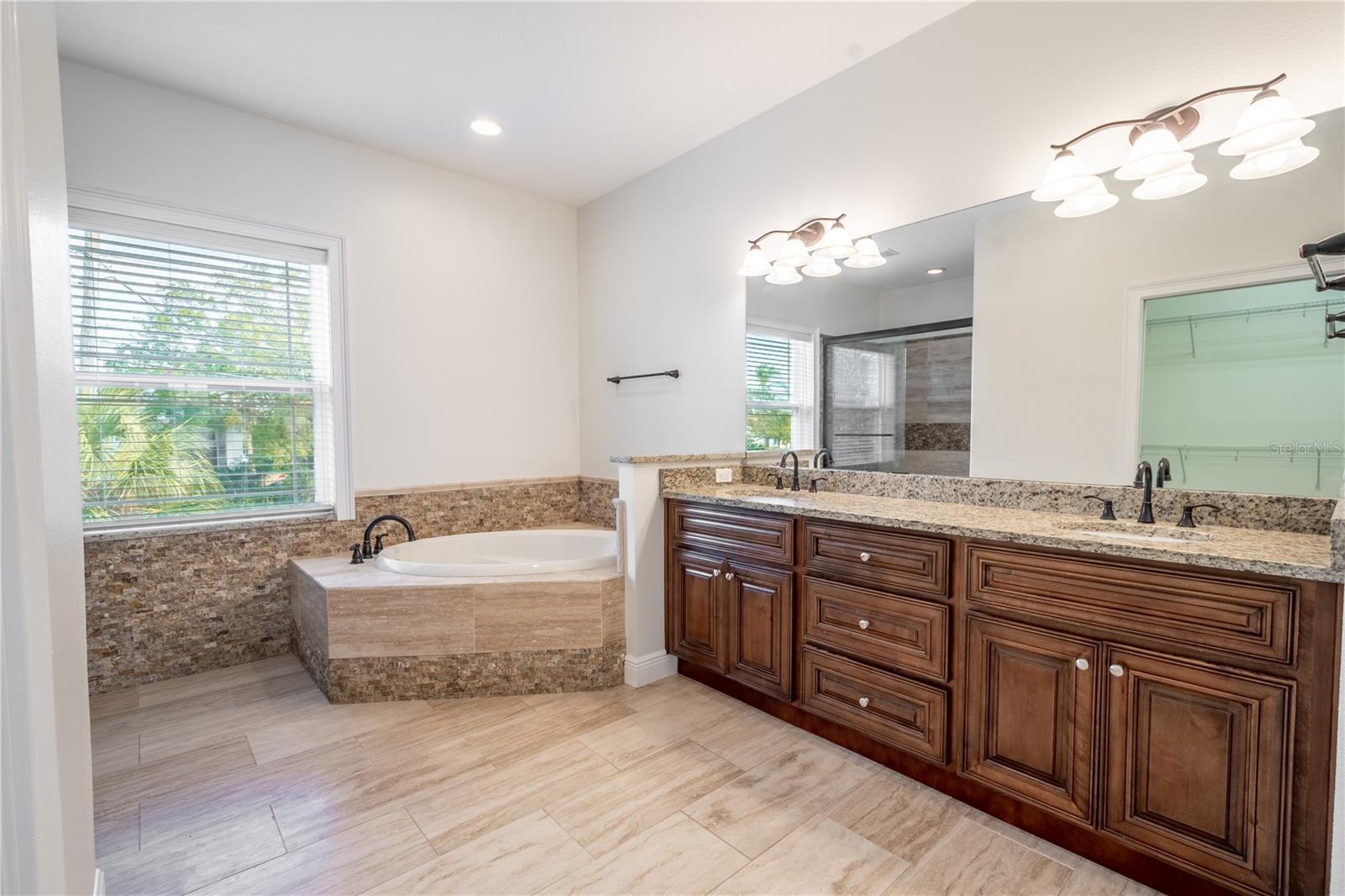 The primary ensuite has polished travertine flooring, a dual sink, mirrored solid wood vanity with storage, granite countertops and down light fixtures.