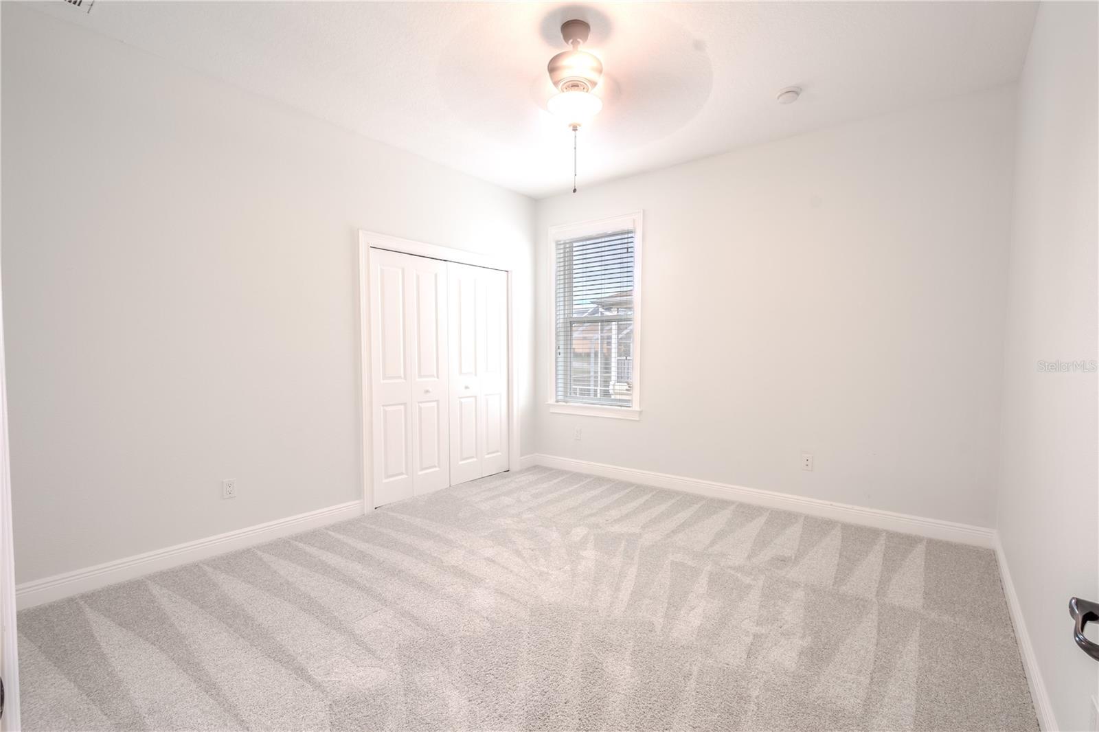 3rd bedroom features a new, neutral-tone carpet and walls, a built-in closet, a ceiling fan, and window blinds.