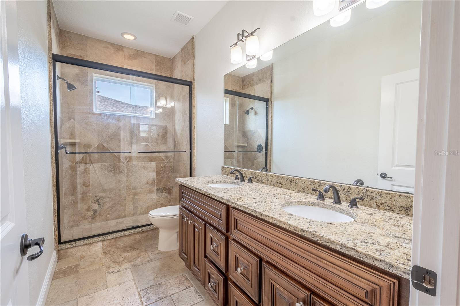 The 3rd bathroom features travertine flooring, a mirrored, dual sink solid wood vanity with granite countertop and down light fixtures and a glass enclosed, tiled walk-in shower.