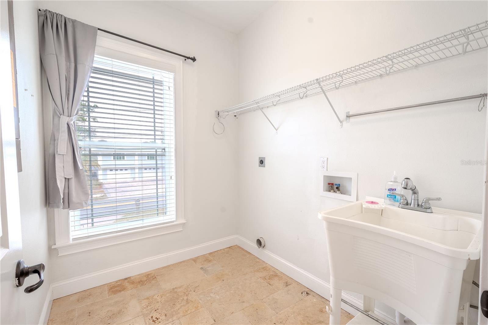 The laundry room features travertine flooring, a utility sink, shelving and hook-ups for your washer and dryer.