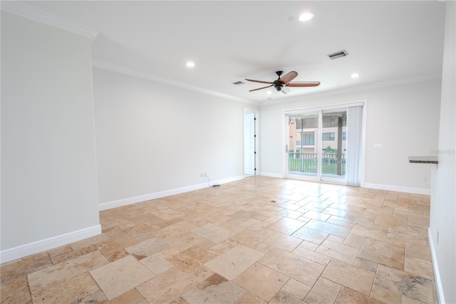 The living room is spacious and inviting, with a neutral color palette and travertine flooring. It has a ceiling fan to keep the room cool and comfortable.