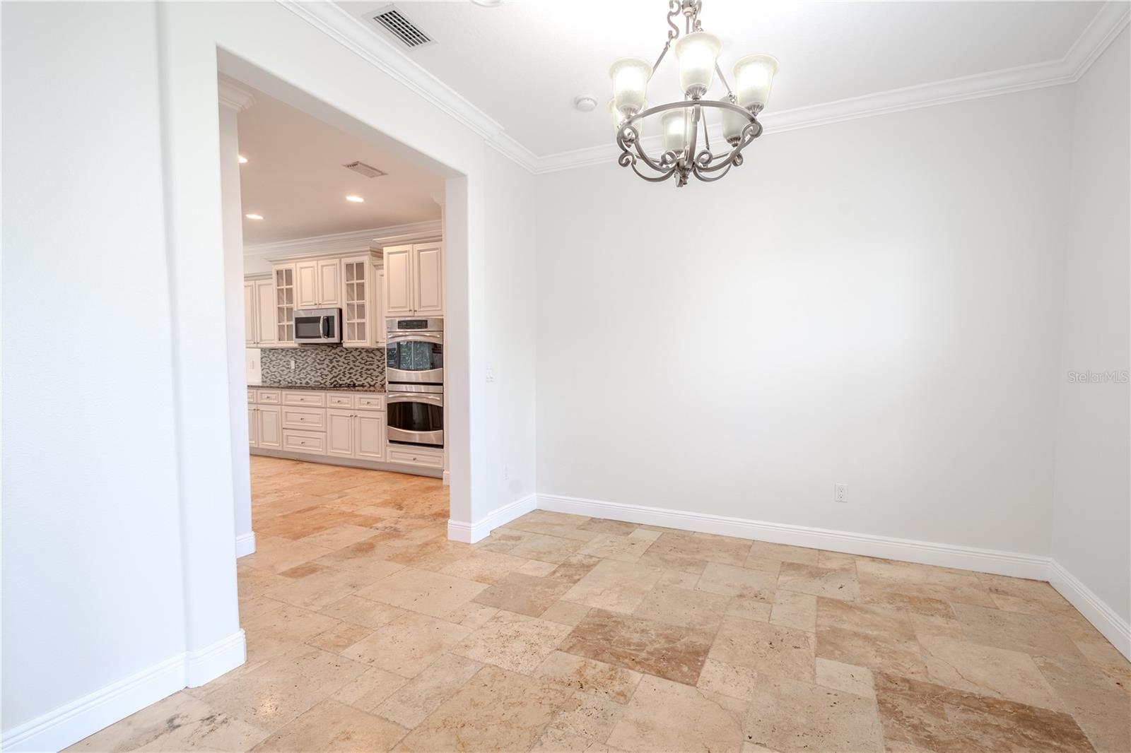 The dining room features travertine flooring, crown molding, and a 6-light Bell Shade Chandelier Lamp.