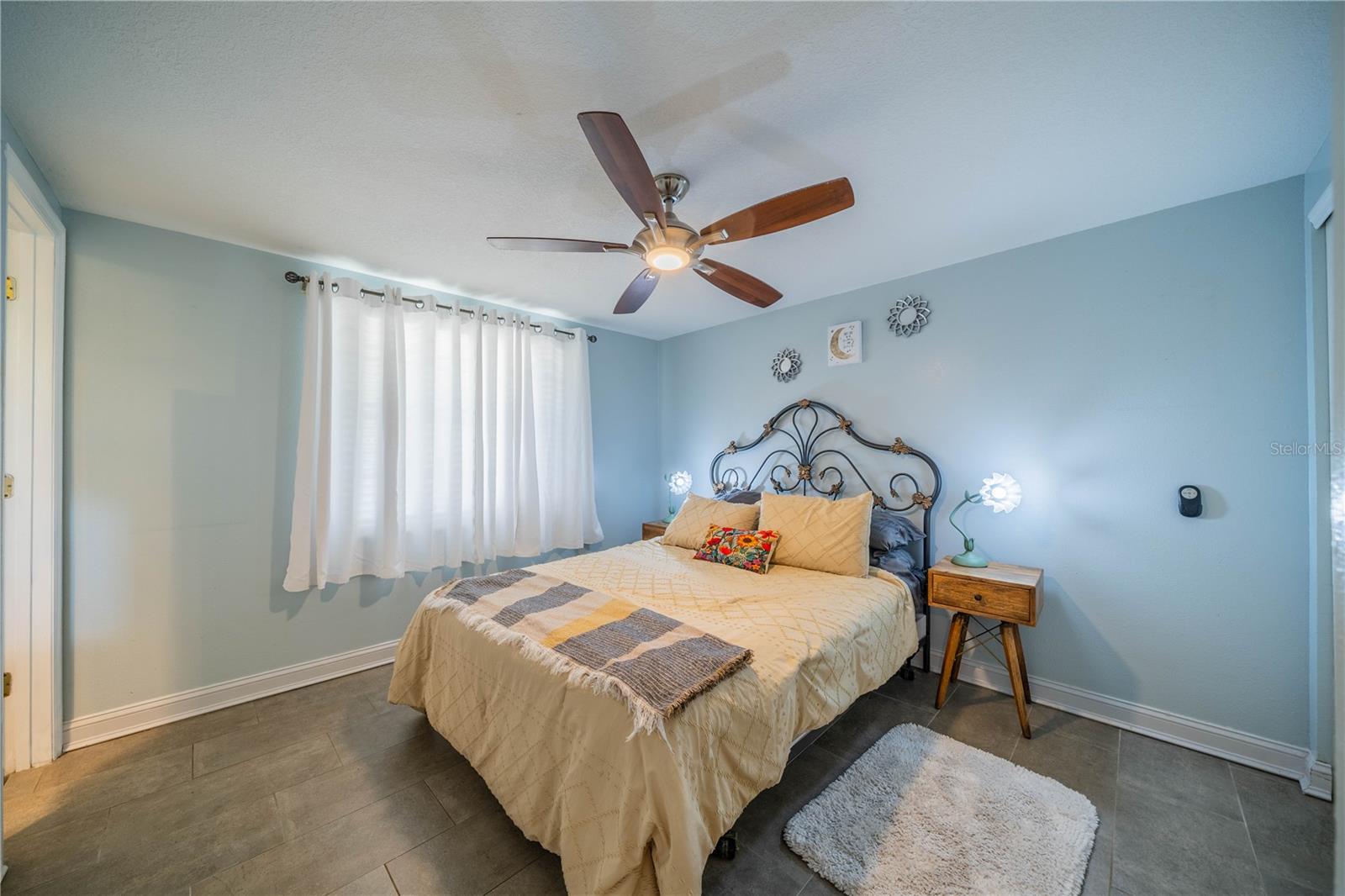 PRIMARY BEDROOM WITH TILE FLOORING, CEILING FAN AND WINDOW TREATMENTS