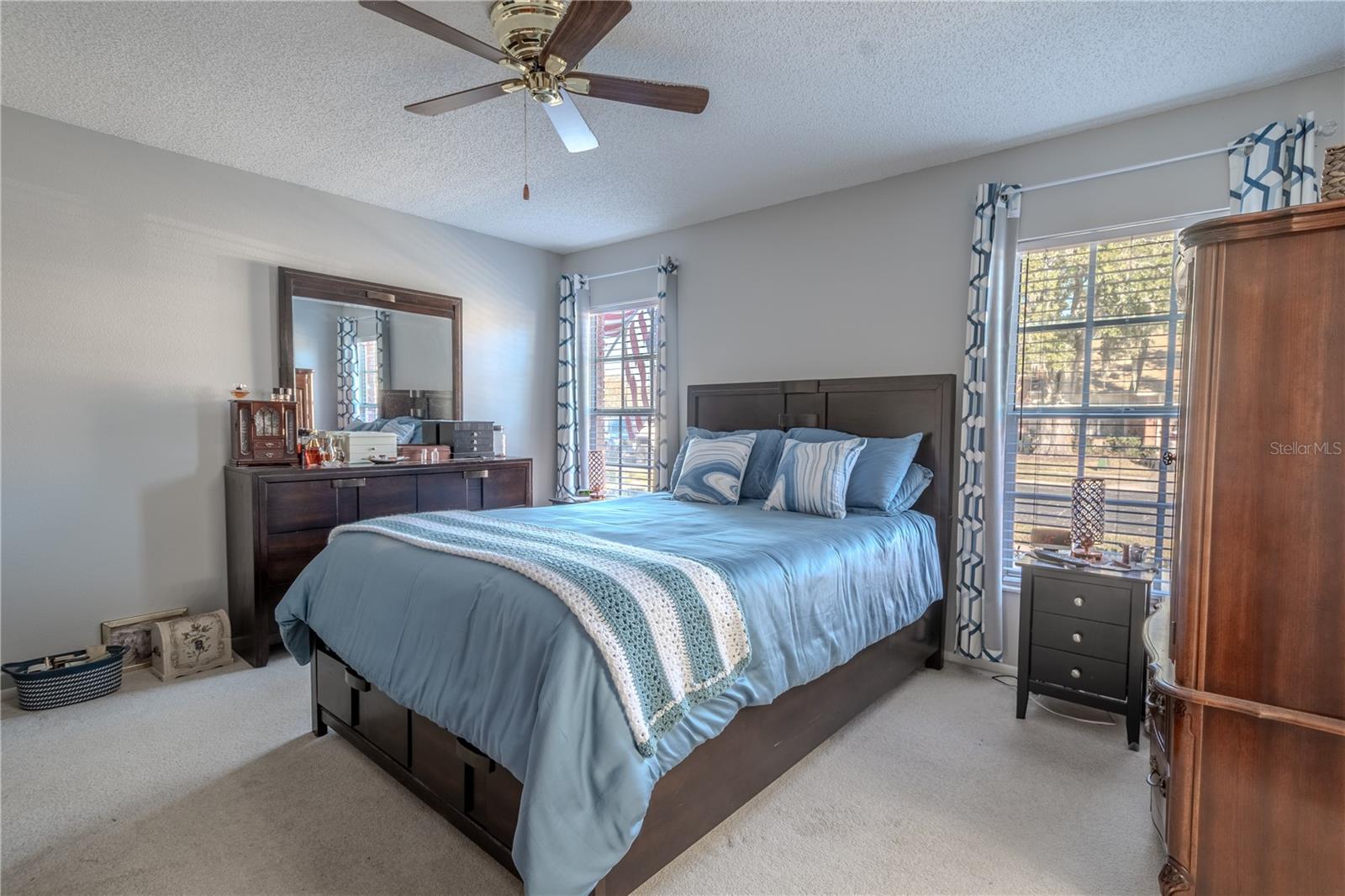 The Primary bedroom features neutral tones, carpet, a ceiling fan with light kit, dual walk-in closets and an ensuite bath.