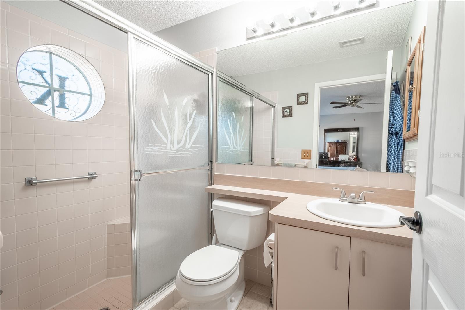 The primary ensuite bath features a mirrored vanity with storage, and a walk in shower with built in bench and ceramic tile floor.