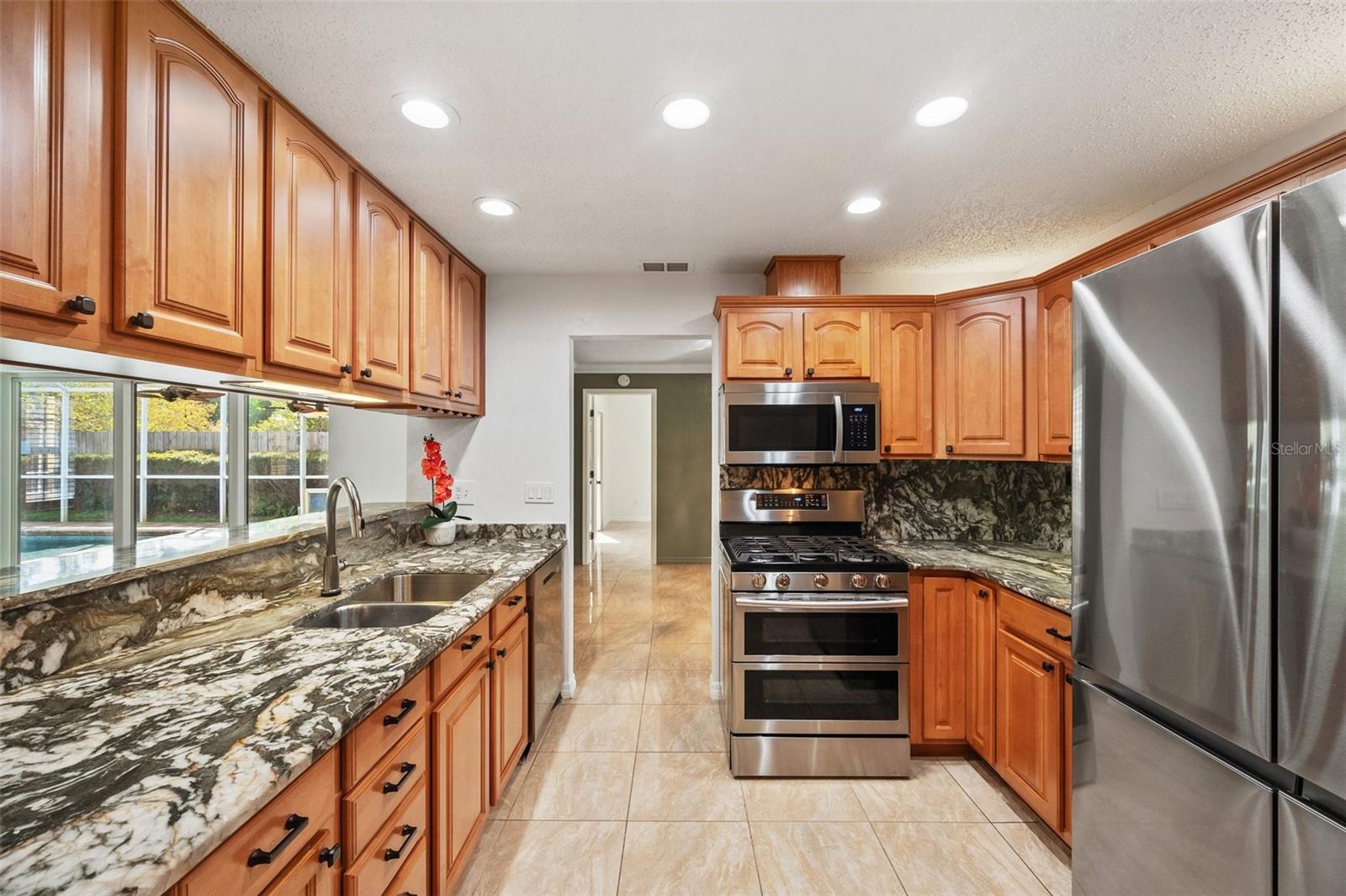 Kitchen graced with granite countertops, maple cabinetry, Samsung appliances, natural gas range with dual ovens, Voice controlled faucet, great view of pool and fireplace. .