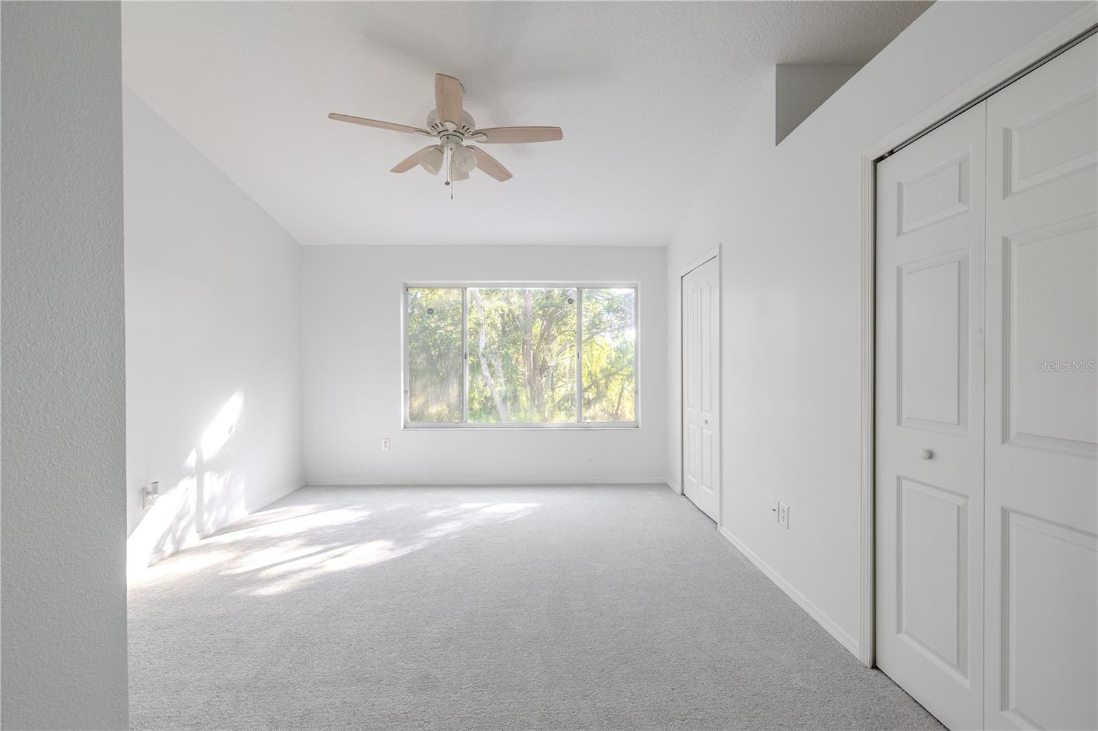The Primary bedroom  features neutral tone walls and carpet, a ceiling fan with light kit and vaulted ceiling.