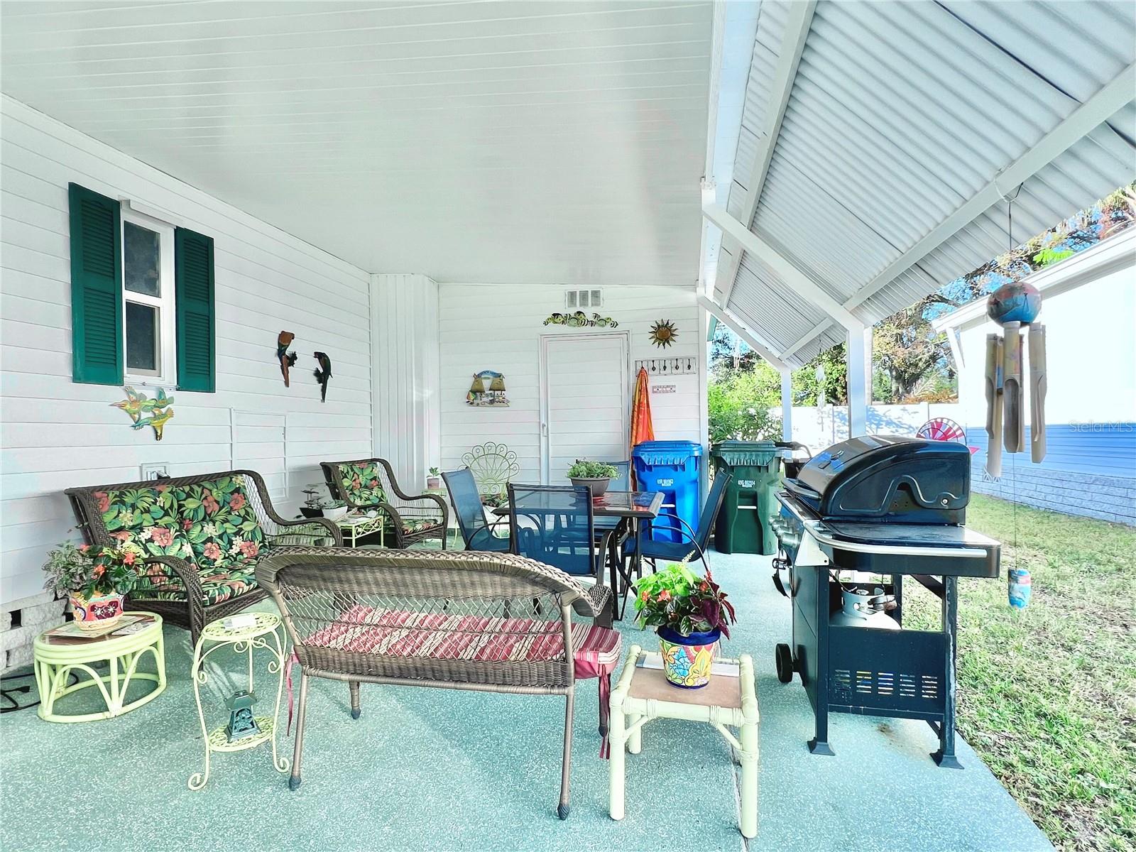 Sitting area under carport with patio furniture and grill.