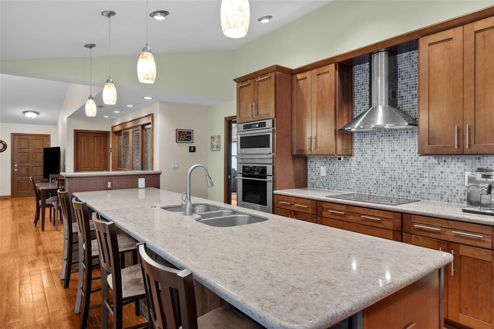 This kitchen has a large island with an eating area. The island has a granite countertop, triple sinks and seating for four.