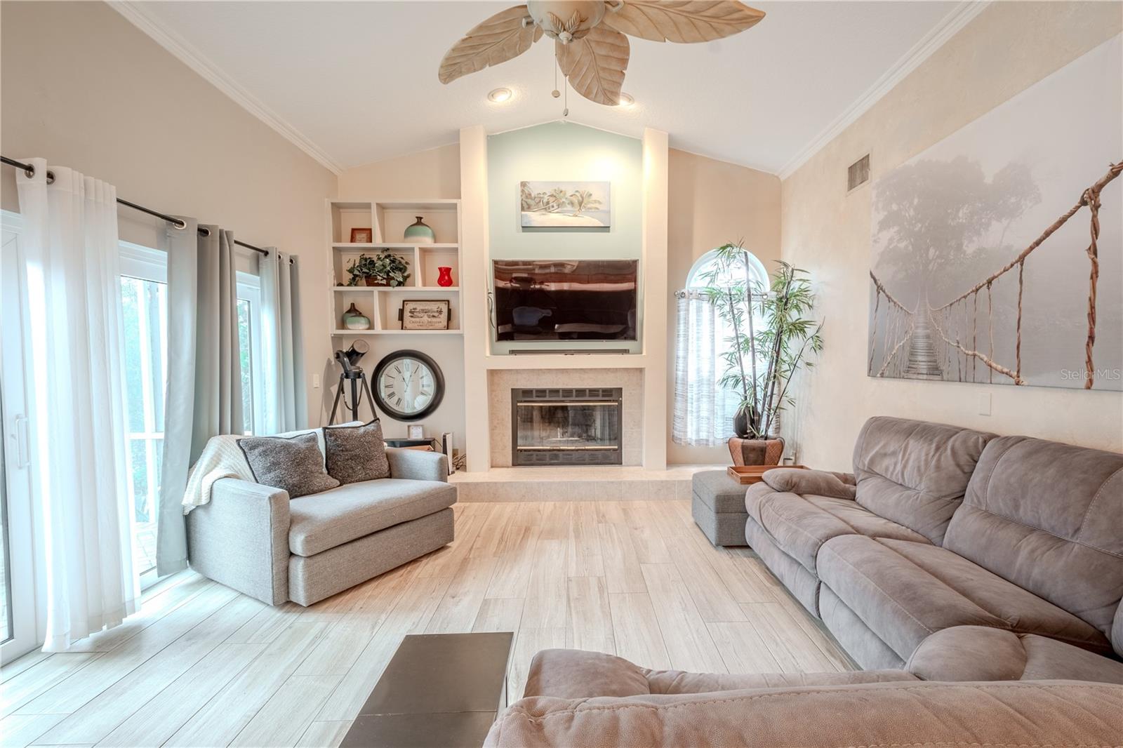 The family room has wood look porcelain tile, high ceilings, a ceiling fan and hurricane impact sliding glass doors to the private lanai.