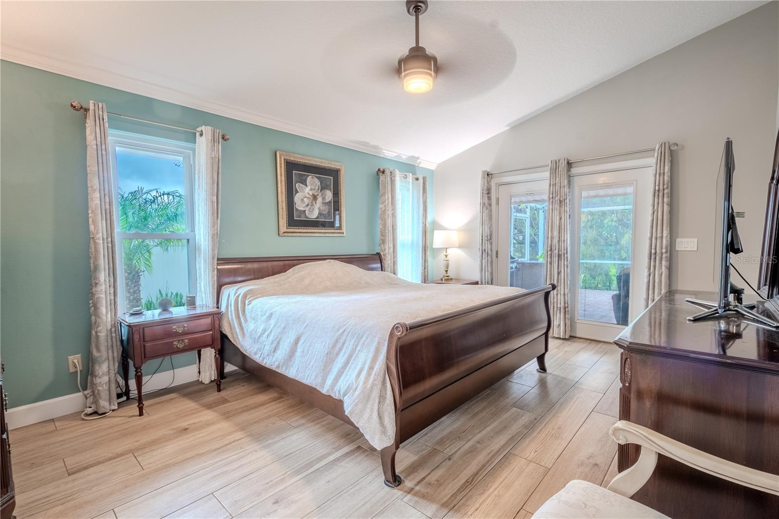 The primary bedroom features a vaulted ceiling with ceiling fan, wood-look porcelain tile floor and french doors to the lanai.