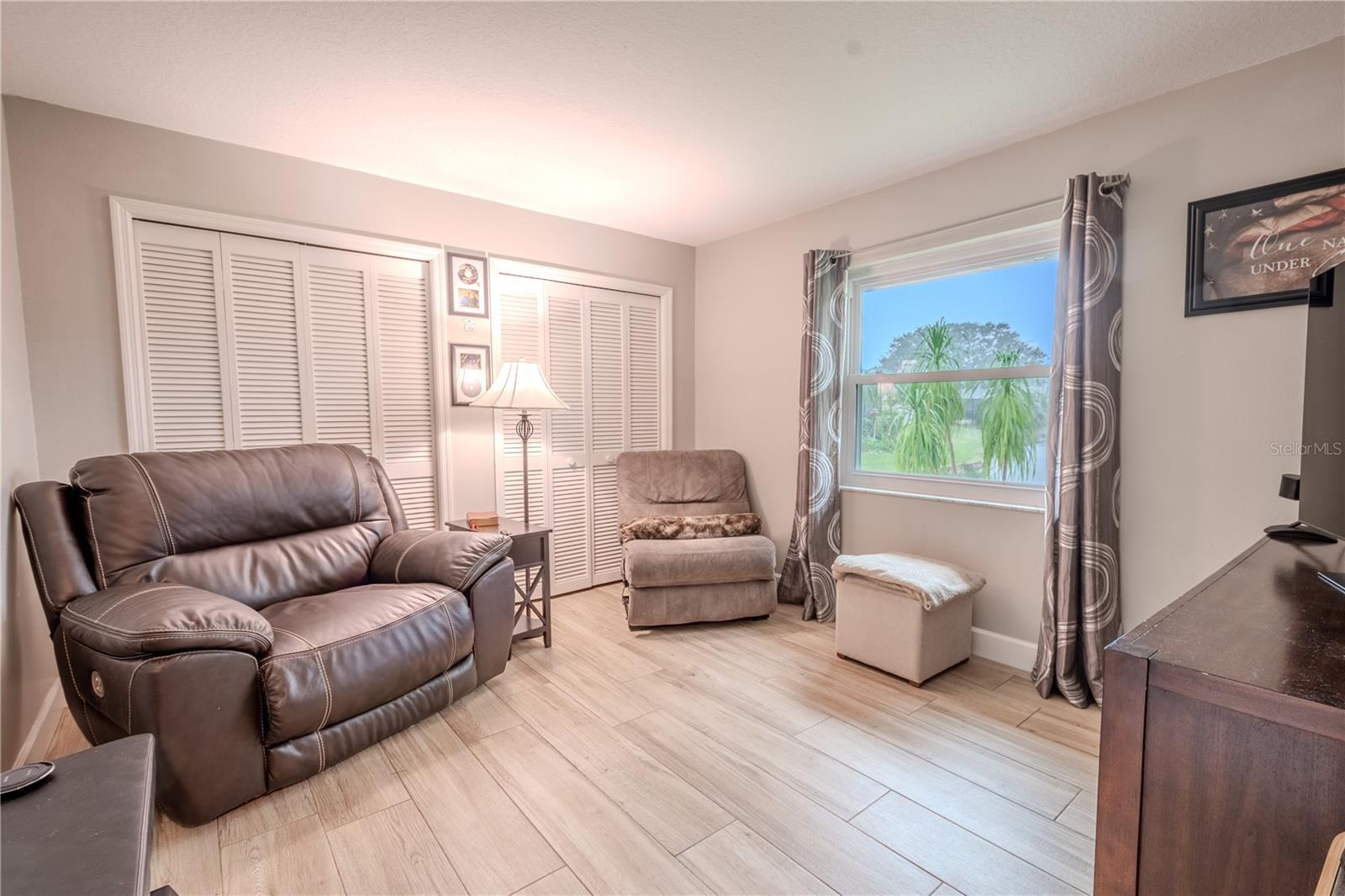 Bedroom 2, currently used as a den, features wood-look porcelain tile and dual built in closets with shutter doors.