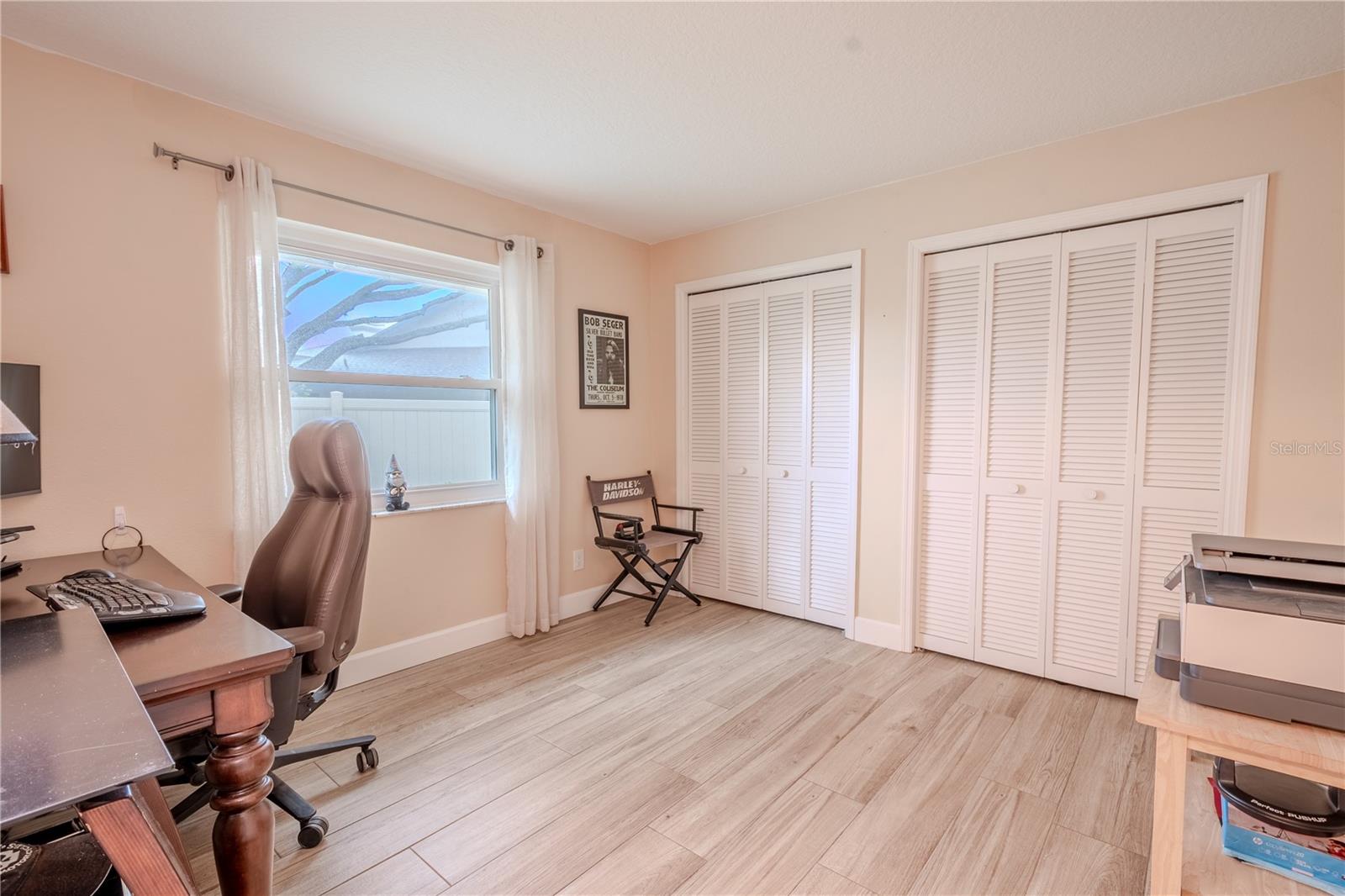 Bedroom 3, currently used as a home office, features wood-look porcelain tile and dual built in closets with shutter doors.