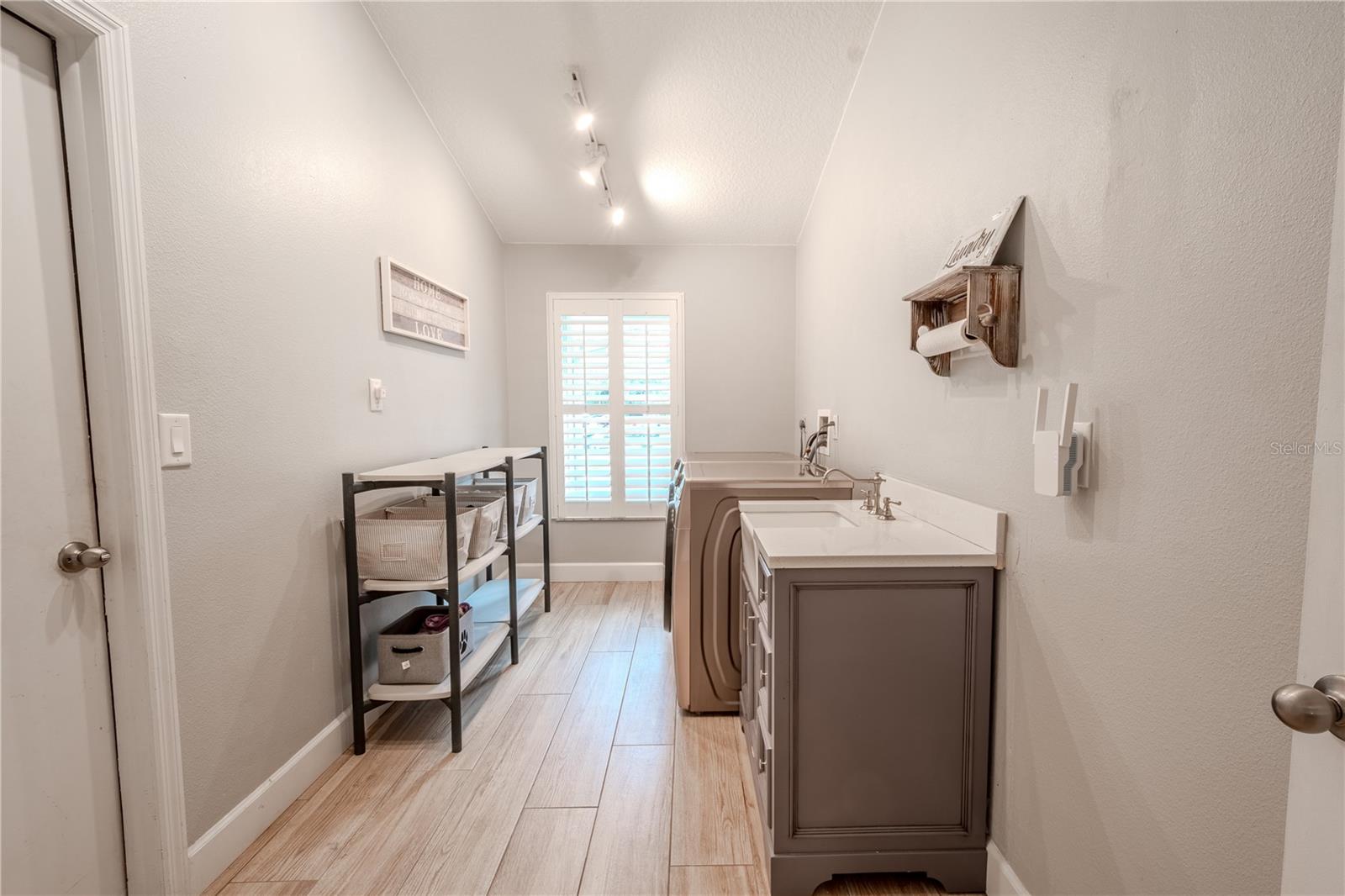 The laundry room is spacious, with a vaulted ceiling, stylish porcelain farm sink and cabinet with storage, porcelain tile flooring and washer/dryer hook-ups.