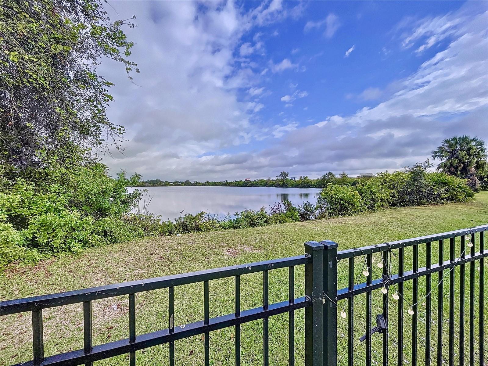 Scenic backyard view overlooking a peaceful lake with lush greenery and a black metal fence