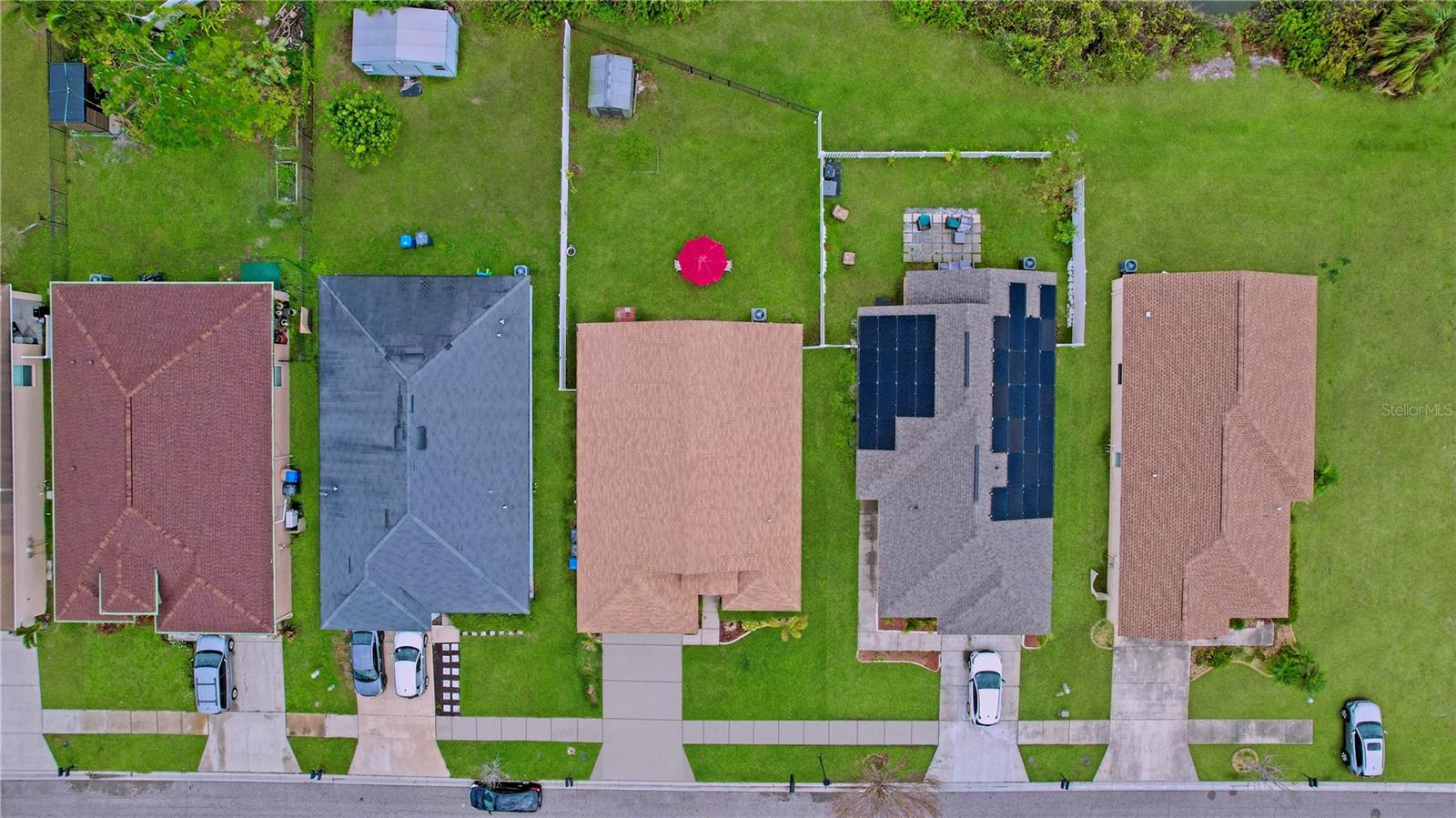 Aerial view of the fenced backyard, featuring patio seating with a red umbrella and storage shed.