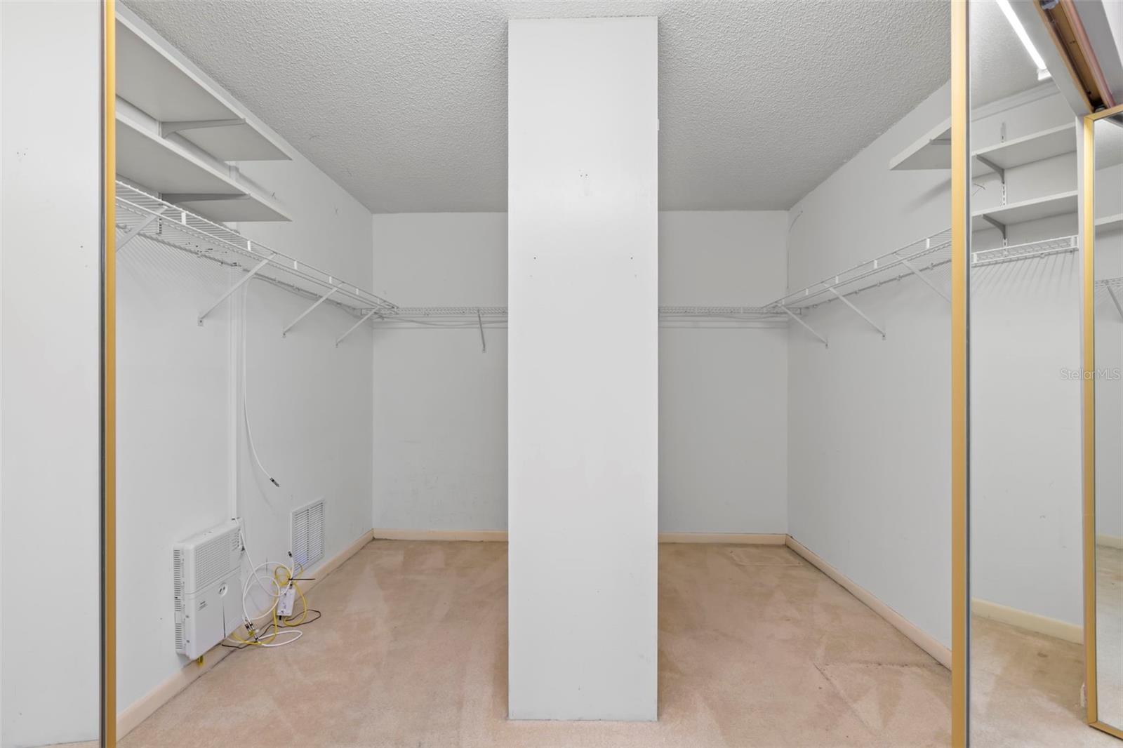 Primary walk-in closet has two sides with floor to ceiling shelves in the middle.