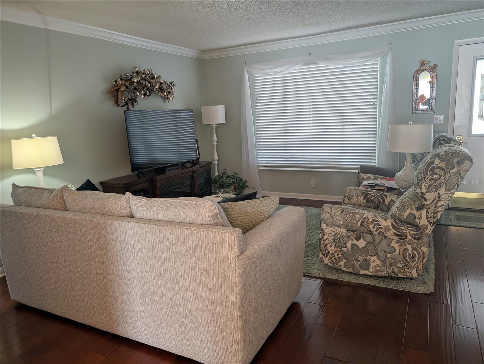 View of living room to front entry. Interior decor has warm tones with coastal flair...crown molding, gorgous wood flooring, faux wood blinds, new interior doors.